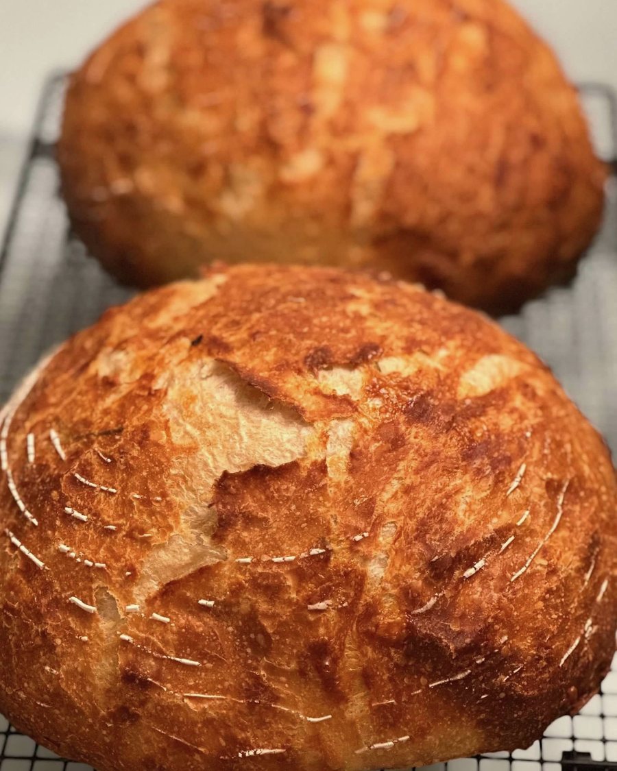 Two deeply golden sourdough boules cooling on a wire rack, hand-scored with a wheat-stalk pattern that has opened up across the crust.