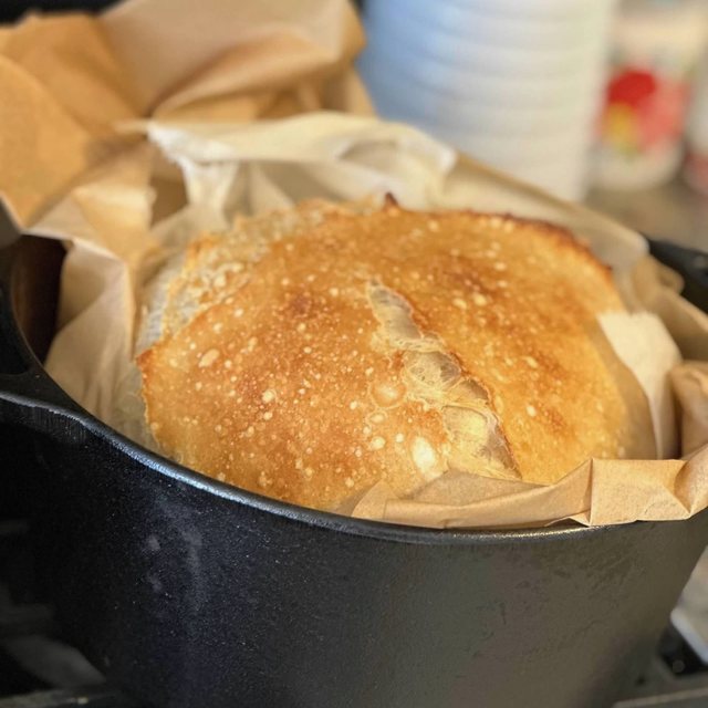 A sourdough loaf baking in a parchment-lined cast iron Dutch oven, its crust turning golden.