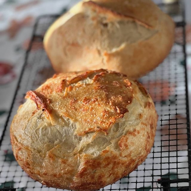 A finished sourdough loaf crusted with baked cheese and herbs, cooling on a wire rack.