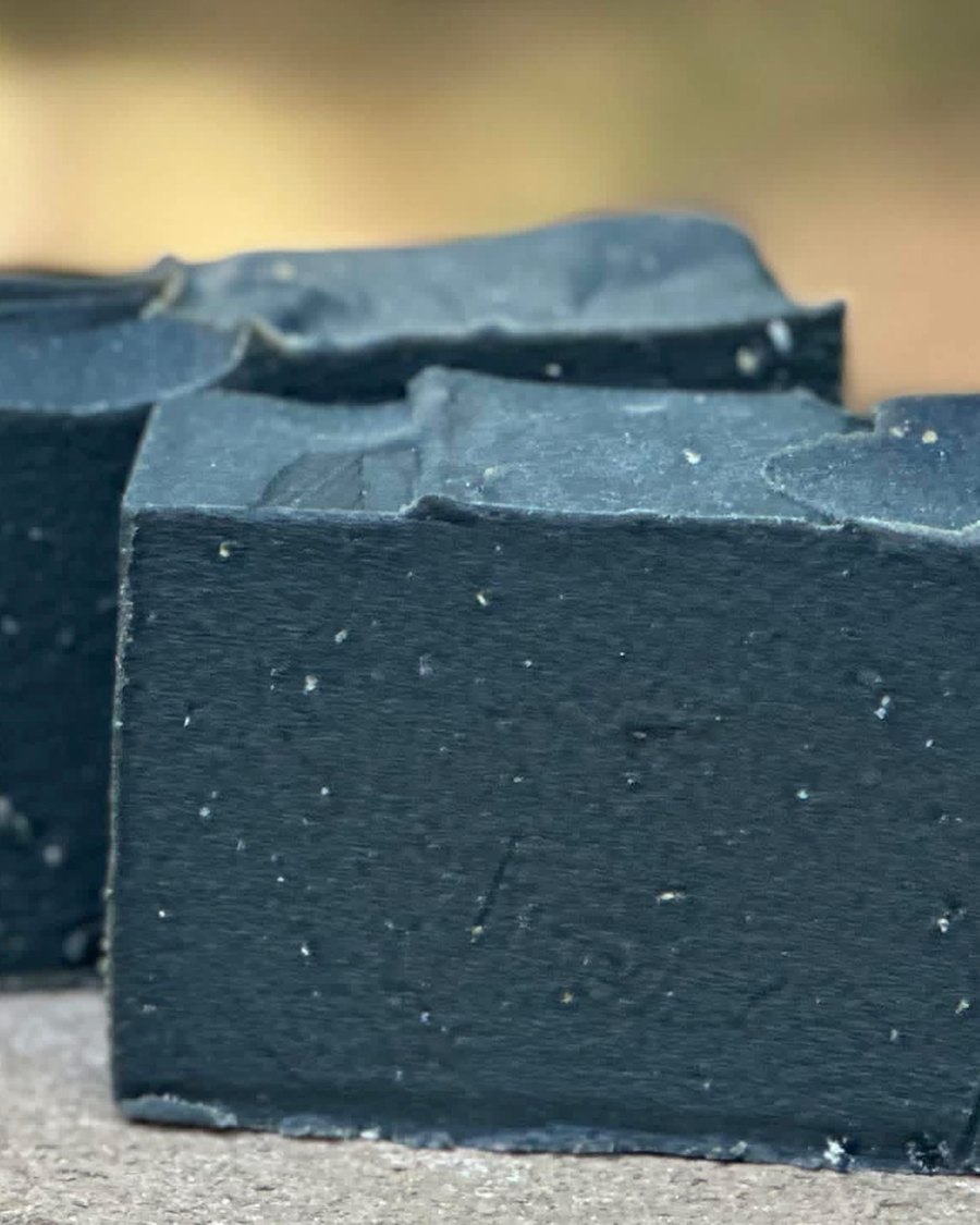 Two bars of hand-cut pine tar soap resting on stone outdoors, dark all the way through, tops left rough where the batter set.