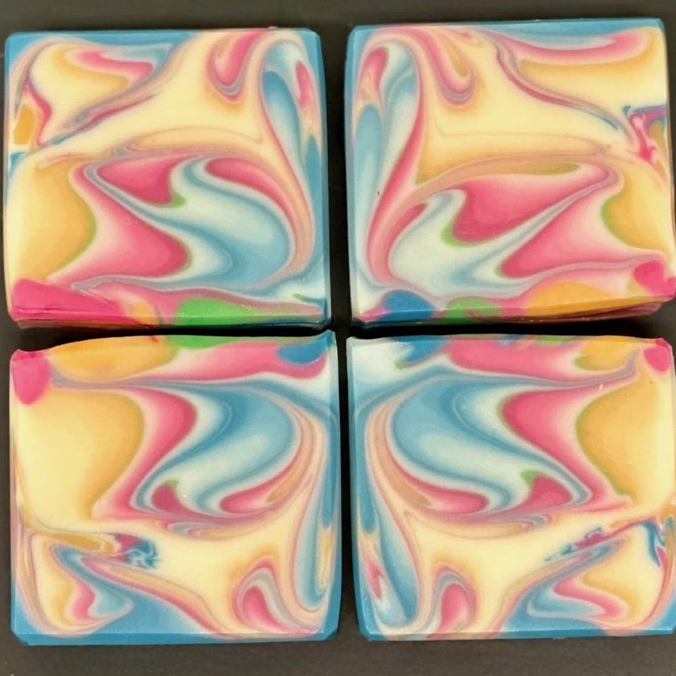 Four cut bars of cold-process soap, each swirled with pink, blue, yellow and green.